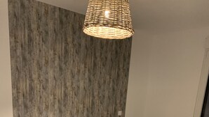 A bedroom with a large bed, a wicker headboard, a wall-mounted light fixture, and a bedside table with a lamp. - Zen Lonora B&B (Créhange)