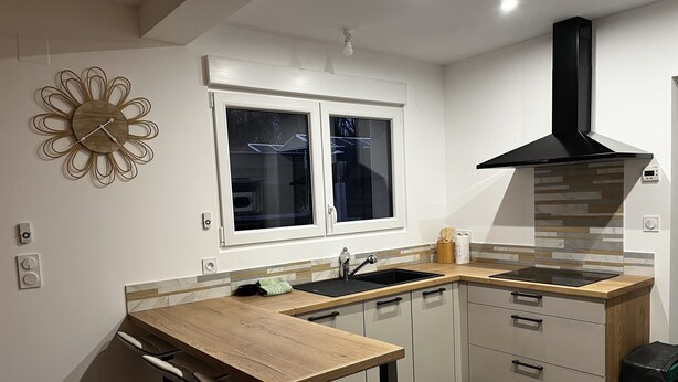 A modern kitchen with a wooden countertop, a black stove, and a window with blinds. - Zen Lonora B&B (Créhange)