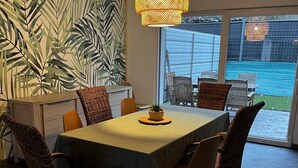 A dining area with a table set for six, surrounded by wicker chairs, a hanging light fixture, and a large window with a view of a backyard. - Zen Lonora B&B (Créhange)