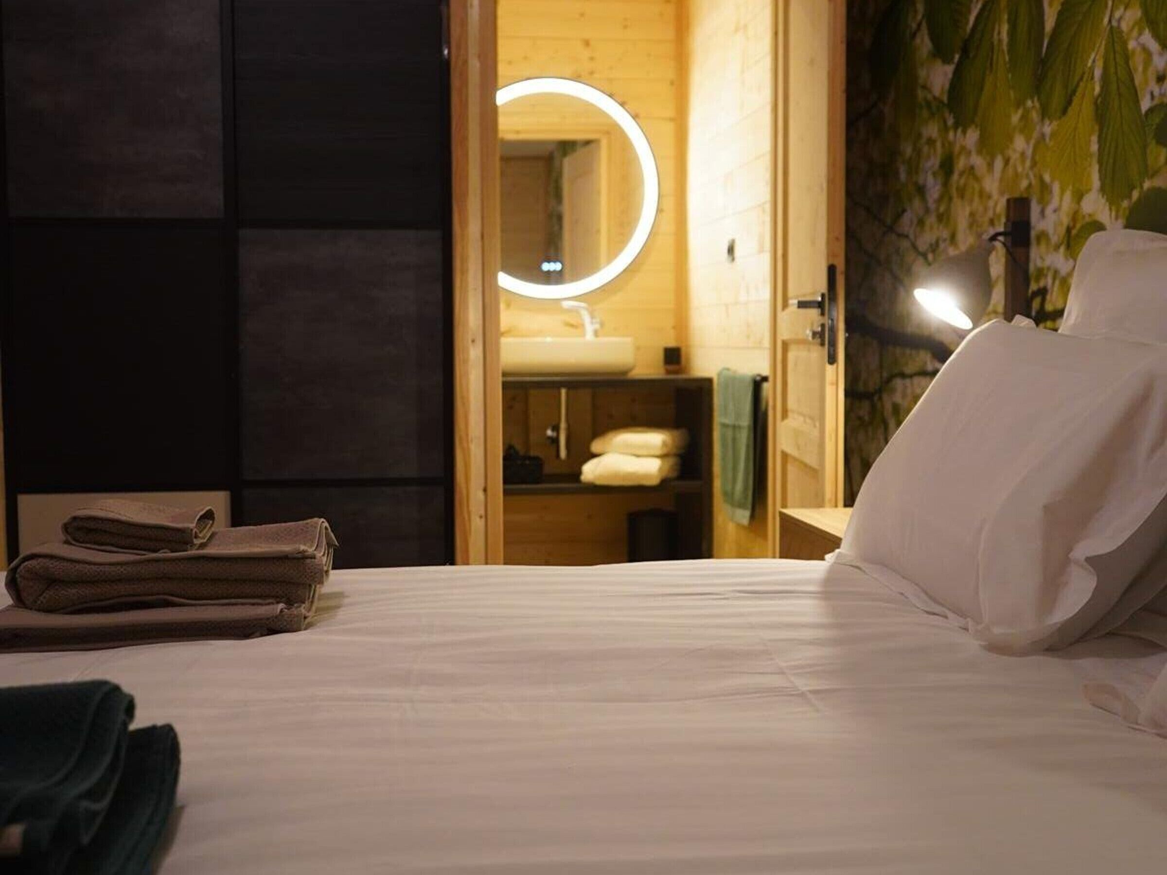 Ein Hotelzimmer mit einem Bett, einer Holztür zu einem Badezimmer und einem Spiegel mit Beleuchtung.