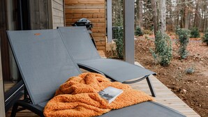Deux fauteuils de jardin sont placés sur une terrasse en bois, et un livre repose sur l’un d’eux.