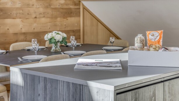 Un comedor con una pared de madera, una mesa dispuesta para cuatro personas con flores blancas, y una caja de queso sobre la mesa.