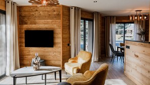 Ein modernes Wohnzimmer mit einer Holzverkleidung, einem Flachbildfernseher, einem Couchtisch, zwei Sesseln und einem Sofa.