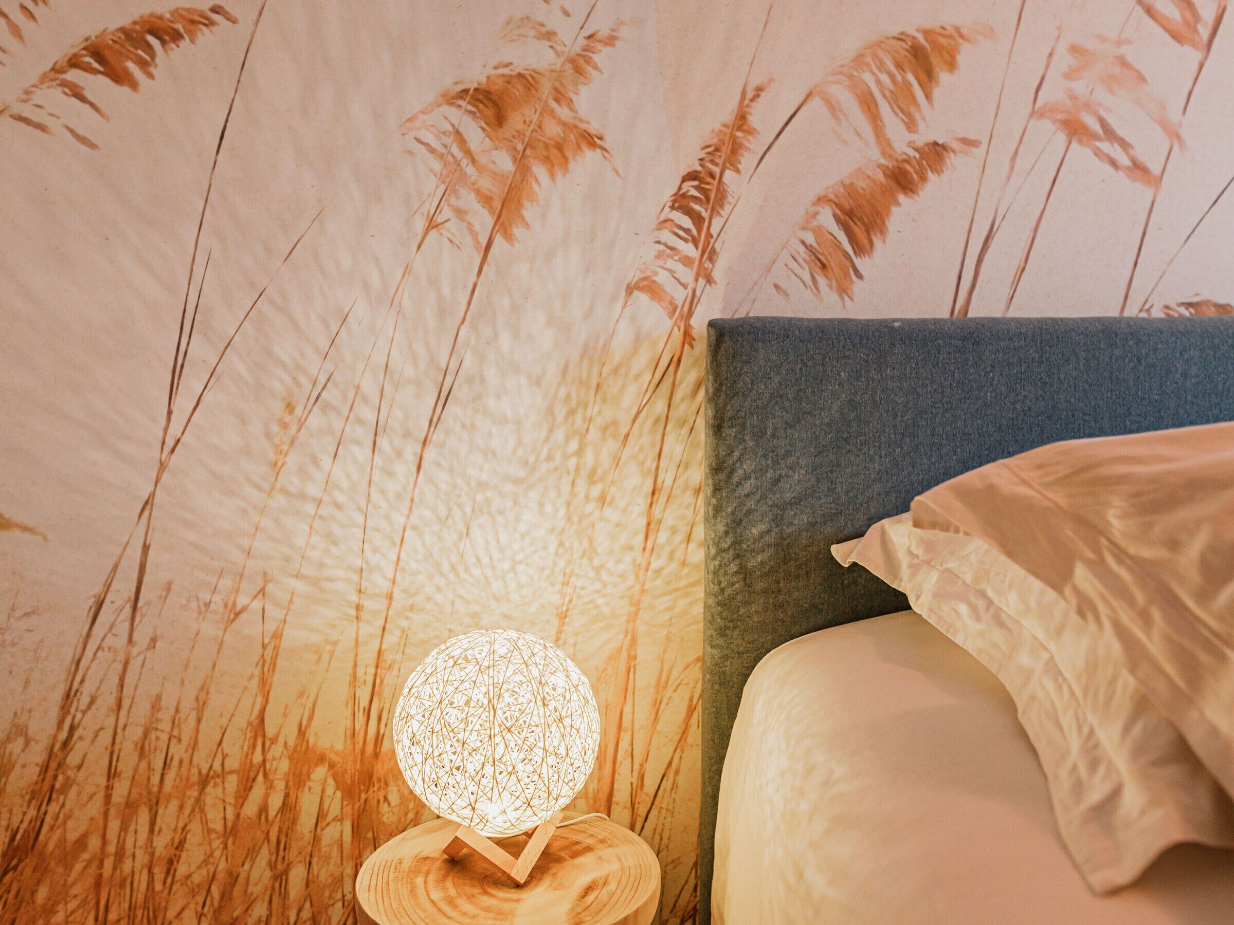 A bedroom with a bed, a nightstand with a spherical lamp, and a wall with a wheat field mural.