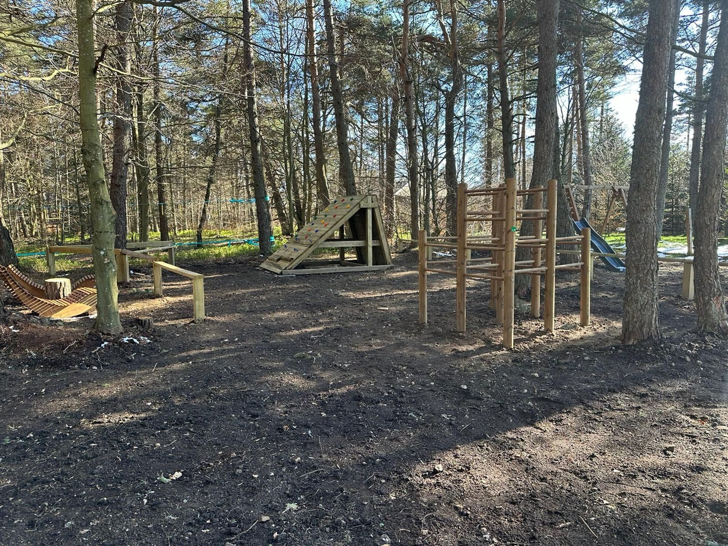 Une aire de jeux avec un toboggan, des structures d’escalade et un banc en bois.