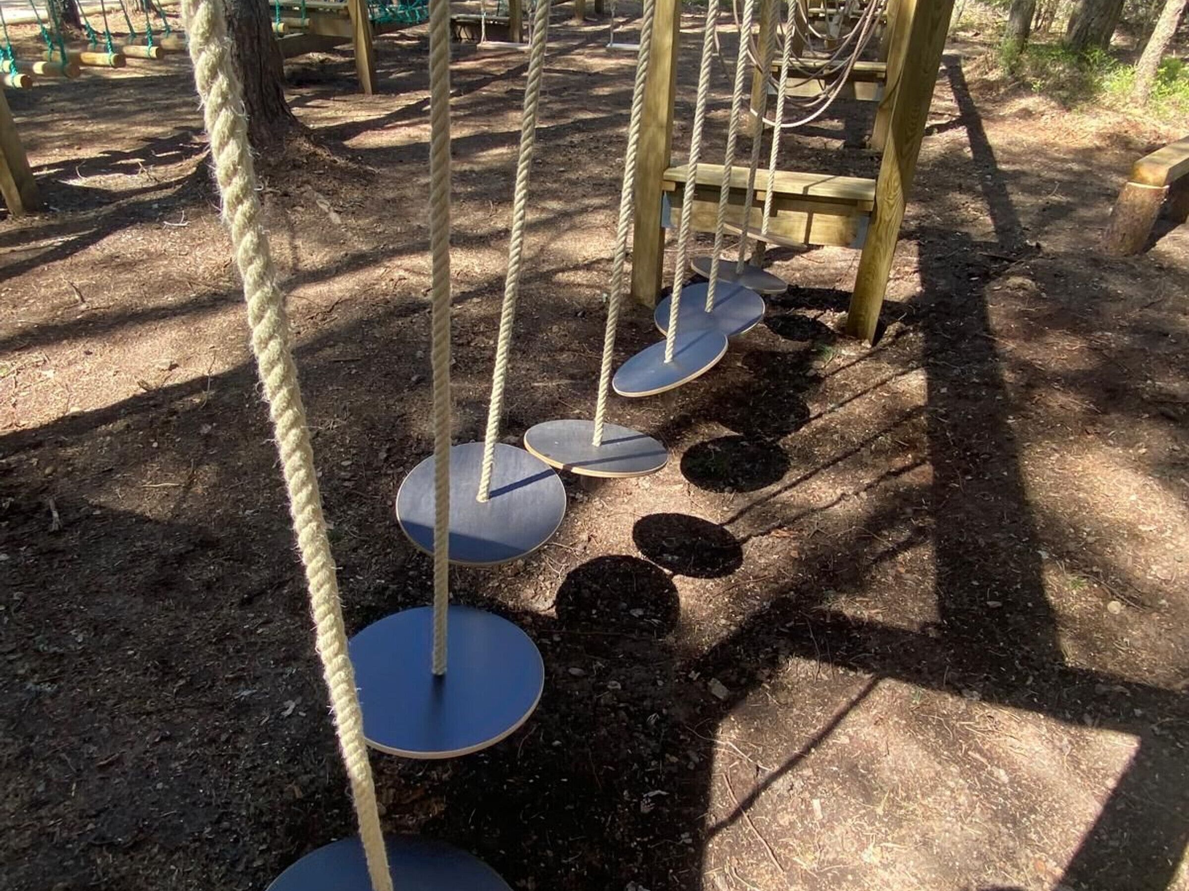 Un parque infantil con una estructura de escalada de cuerdas y plataformas circulares.