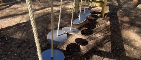 Un parque infantil con una estructura de escalada de cuerdas y plataformas circulares.