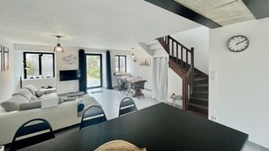 Una sala de estar moderna con sofá, mesa de comedor y sillas. Se ve una escalera que sube a otro nivel.