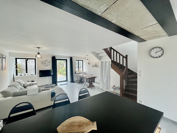 A modern living room with a sofa, dining table, and chairs. There is a staircase leading to another level.