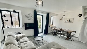 Una sala de estar moderna con un sofá seccional, una mesa de comedor con sillas, un televisor montado en la pared y un ventanal con cortinas.
