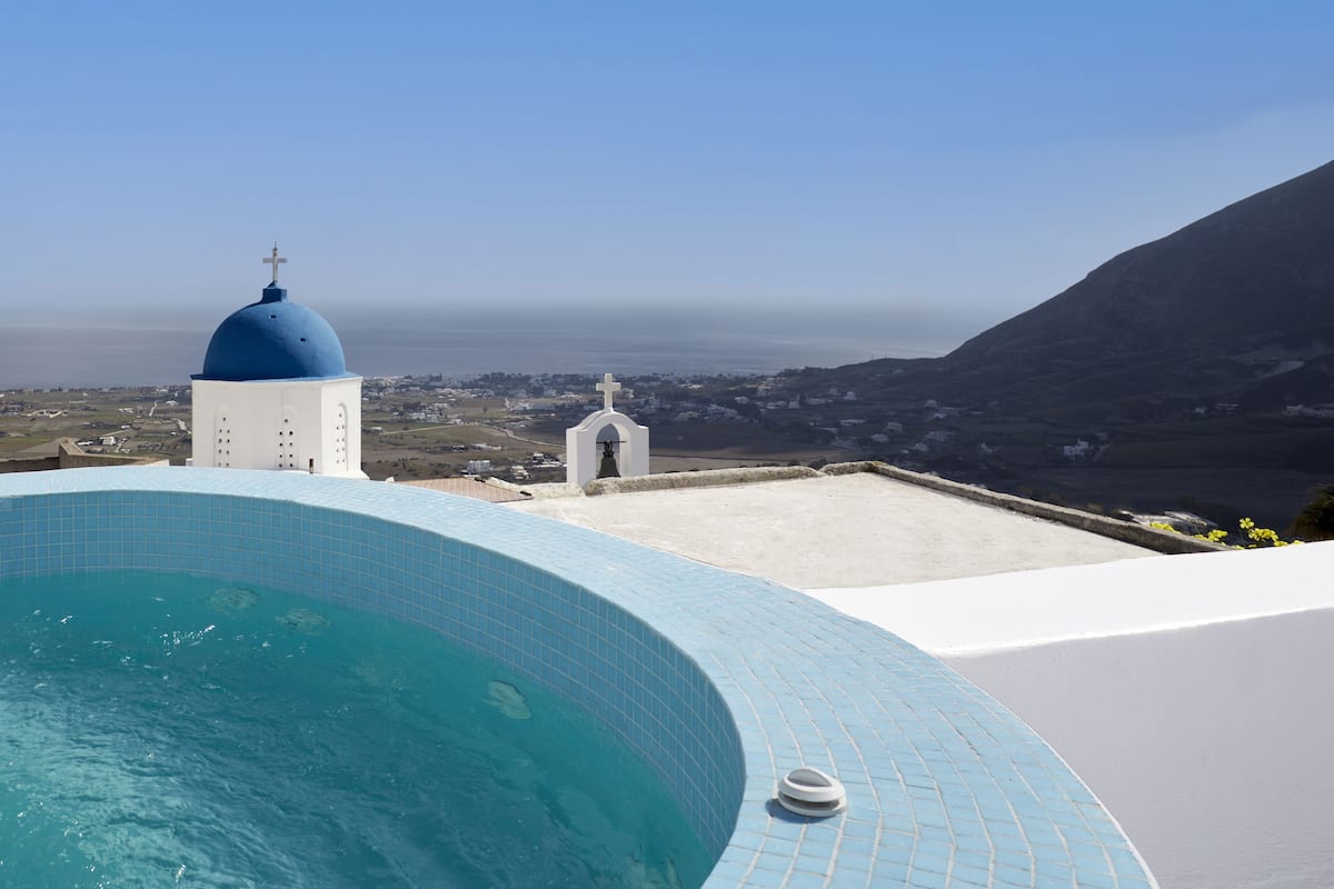 A pool with a blue dome and a white building with a cross, overlooking a coastal landscape.