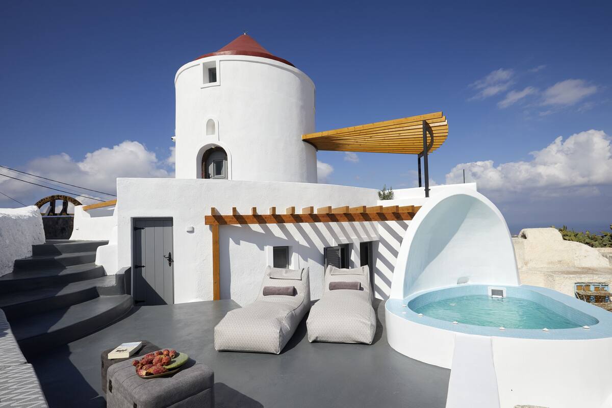 A modern outdoor lounge area with a hot tub, two cushioned seating areas, and a staircase leading to a door.