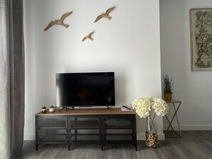 Un salon moderne avec un téléviseur à écran plat posé sur une console en bois, une plante décorative et des œuvres d’art mural.