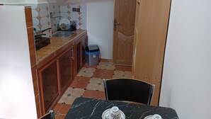 A compact kitchen with a sink, stove, and cabinets. A trash bin is visible near the door.