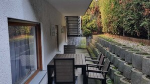 A covered outdoor patio with a table and chairs, a staircase leading to a higher level, and a garden with stone planters.