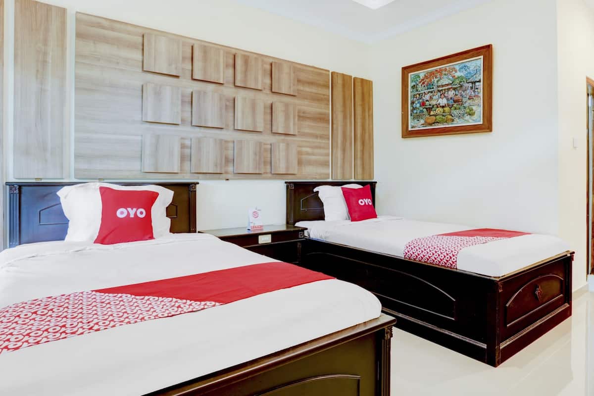 A hotel room with two beds, each with a red and white bedspread and pillows, a wooden headboard, and a wall-mounted artwork.