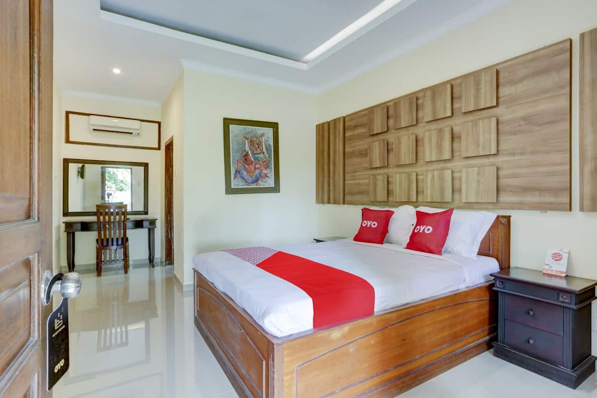 A hotel room with a wooden bed, a desk with a chair, a wall-mounted air conditioner, and a framed picture.