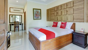 Une chambre d’hôtel avec un lit en bois, un bureau avec une chaise, un climatiseur fixé au mur et un tableau encadré.