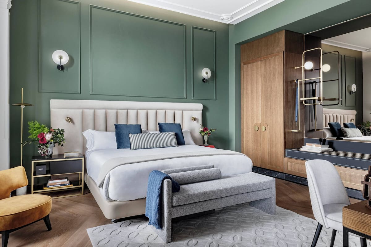 Un dormitorio moderno con una cama grande, un banco, una silla, una mesita de noche y un espejo.