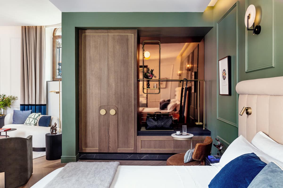 Un dormitorio moderno con una cama grande, un armario, una zona de estar y una mesita de noche con un florero.