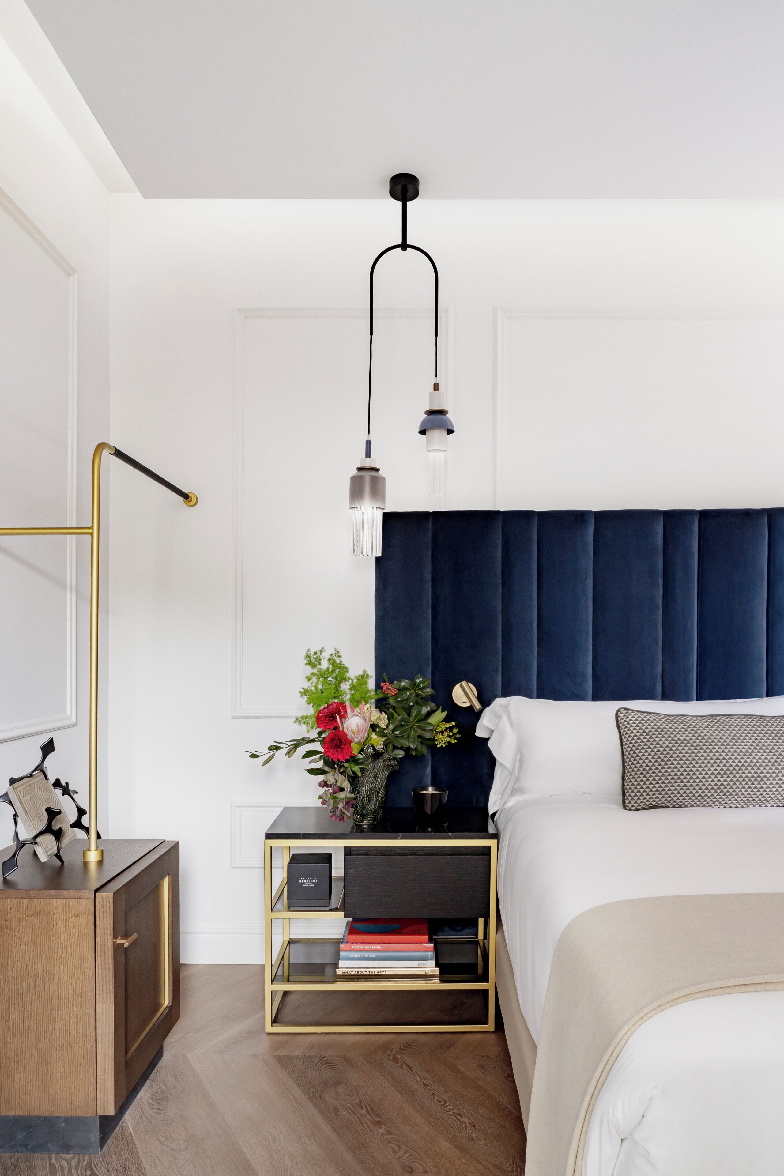 Ein Schlafzimmer mit Bett, Nachttischen, einer Wandlampe und einer Vase mit Blumen.