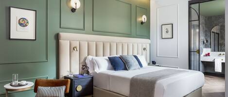 A modern bedroom with a large bed, a nightstand, a chair, and a bathroom visible through an open door.