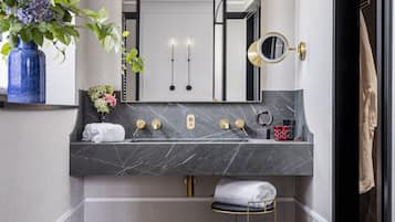 Un baño moderno con encimera de mármol, un espejo grande, un espejo redondo, un perchero y una planta en maceta.