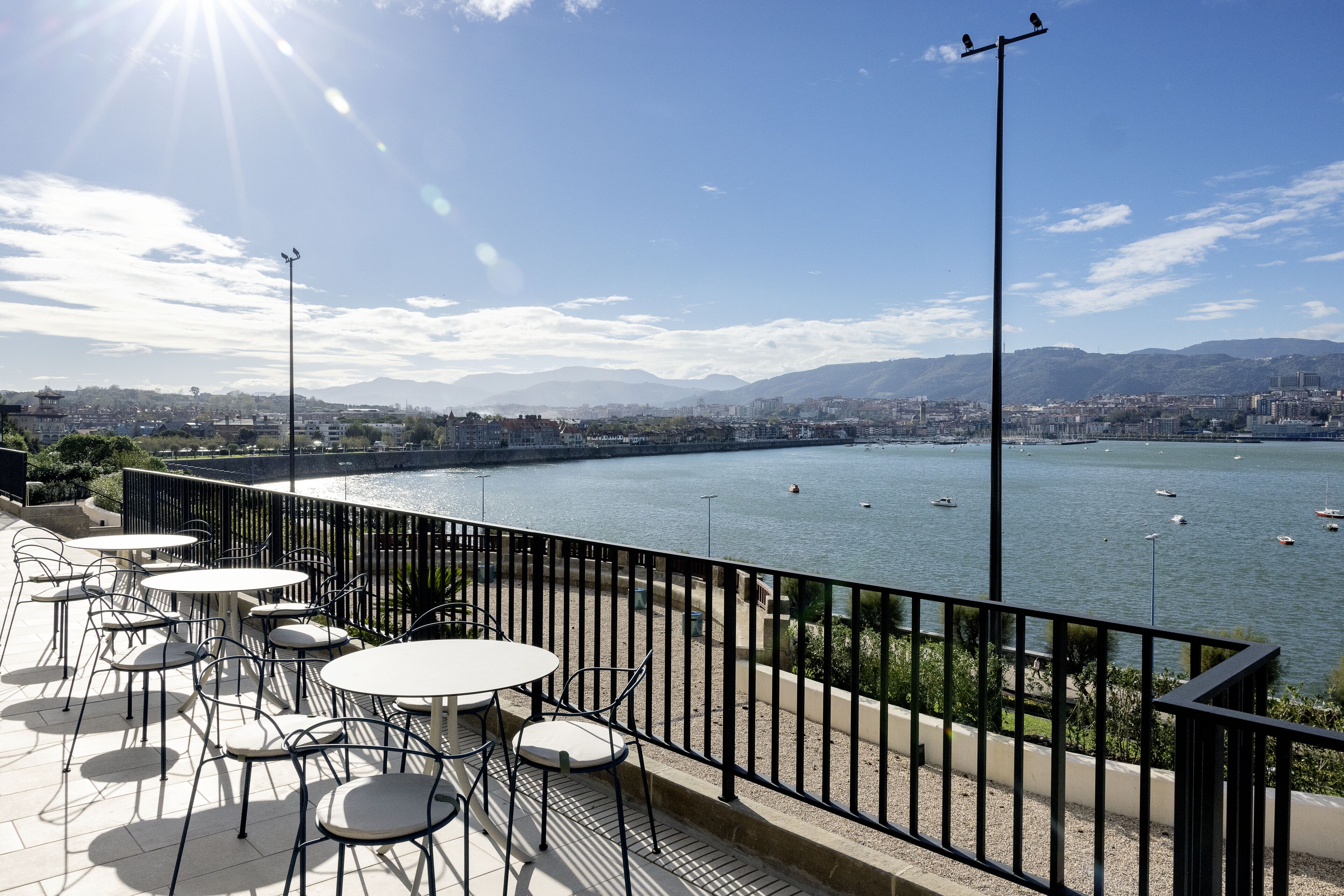 Una terraza con mobiliario exterior que da a un río, con montañas al fondo.