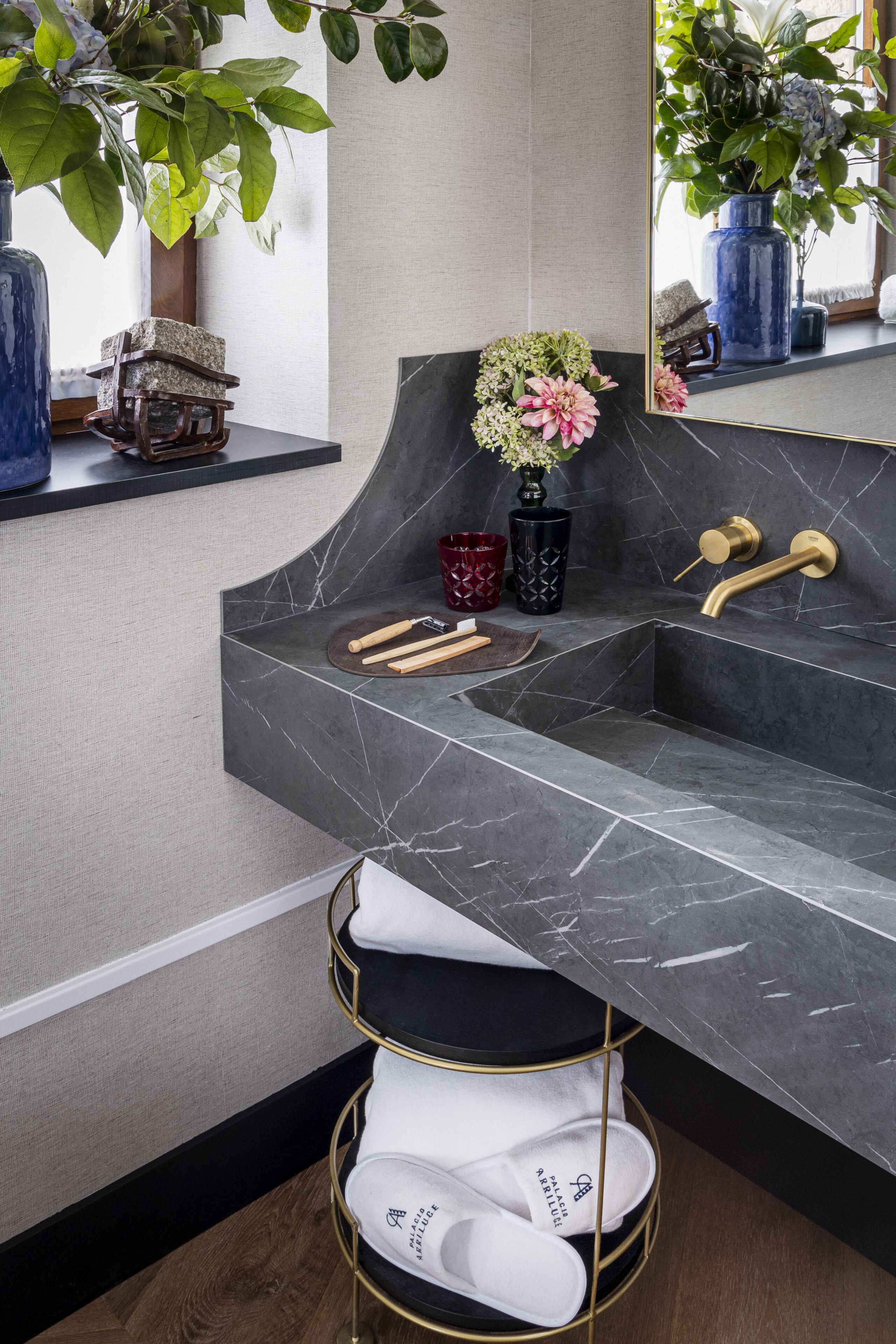 A bathroom with a marble sink, gold faucets, and a mirror. There are plants and decorative items on the counter.