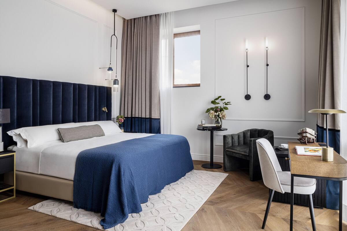 Una habitación de hotel moderna con una cama grande, un escritorio, una silla y una mesita de noche con una lámpara.