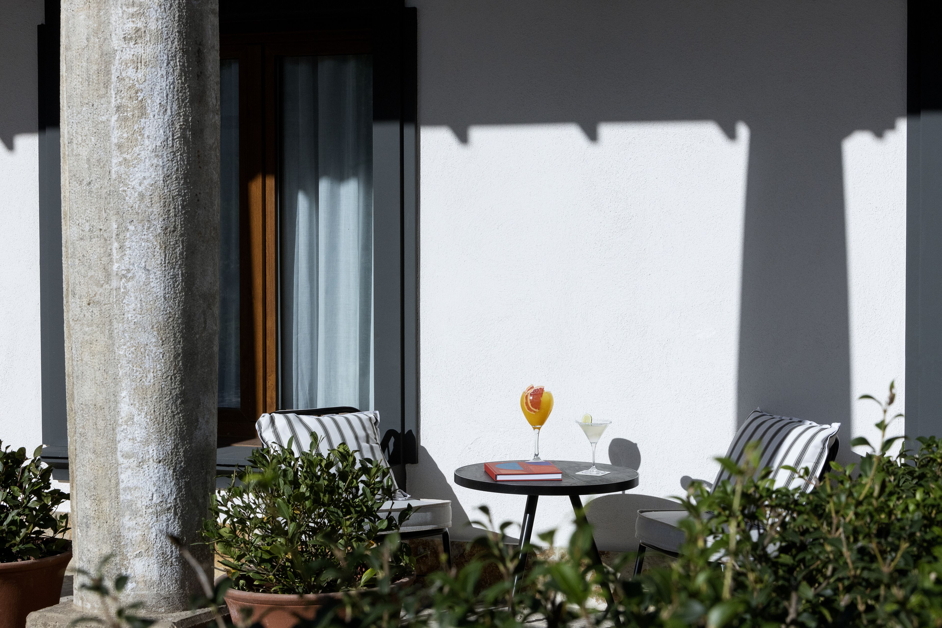 A patio with a round table, two striped chairs, a book, and a cocktail glass.