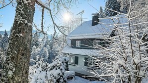 Une maison recouverte de neige, avec un toit en pente, entourée d’arbres et de neige.