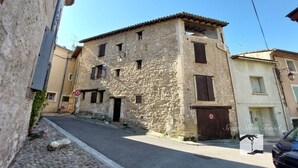 Une rue étroite bordée d’un bâtiment en pierre à l’architecture traditionnelle, avec une grille métallique fermée et une voiture garée.