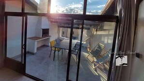 Un balcon avec un barbecue, des chaises et une table.