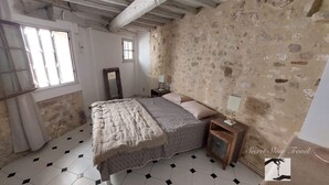Une chambre avec un mur en pierre, un lit recouvert d’une couvre-lit à motifs, une table de chevet avec une lampe et une fenêtre avec des rideaux.