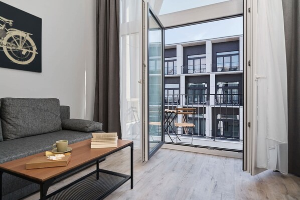 Un salón moderno con sofá, una mesa de centro y un ventanal de vidrio que da a un balcón con vistas a un edificio.