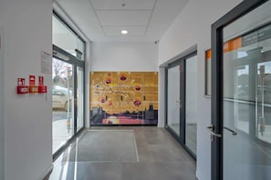 Un couloir avec des portes en verre, un panneau d’indication concernant la sécurité incendie et une fresque murale.