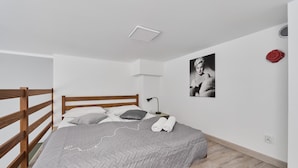 Een slaapkamer met een houten bed, een grijze deken, een nachtkastje met een lamp, een wandheater en een lijst met een afbeelding.