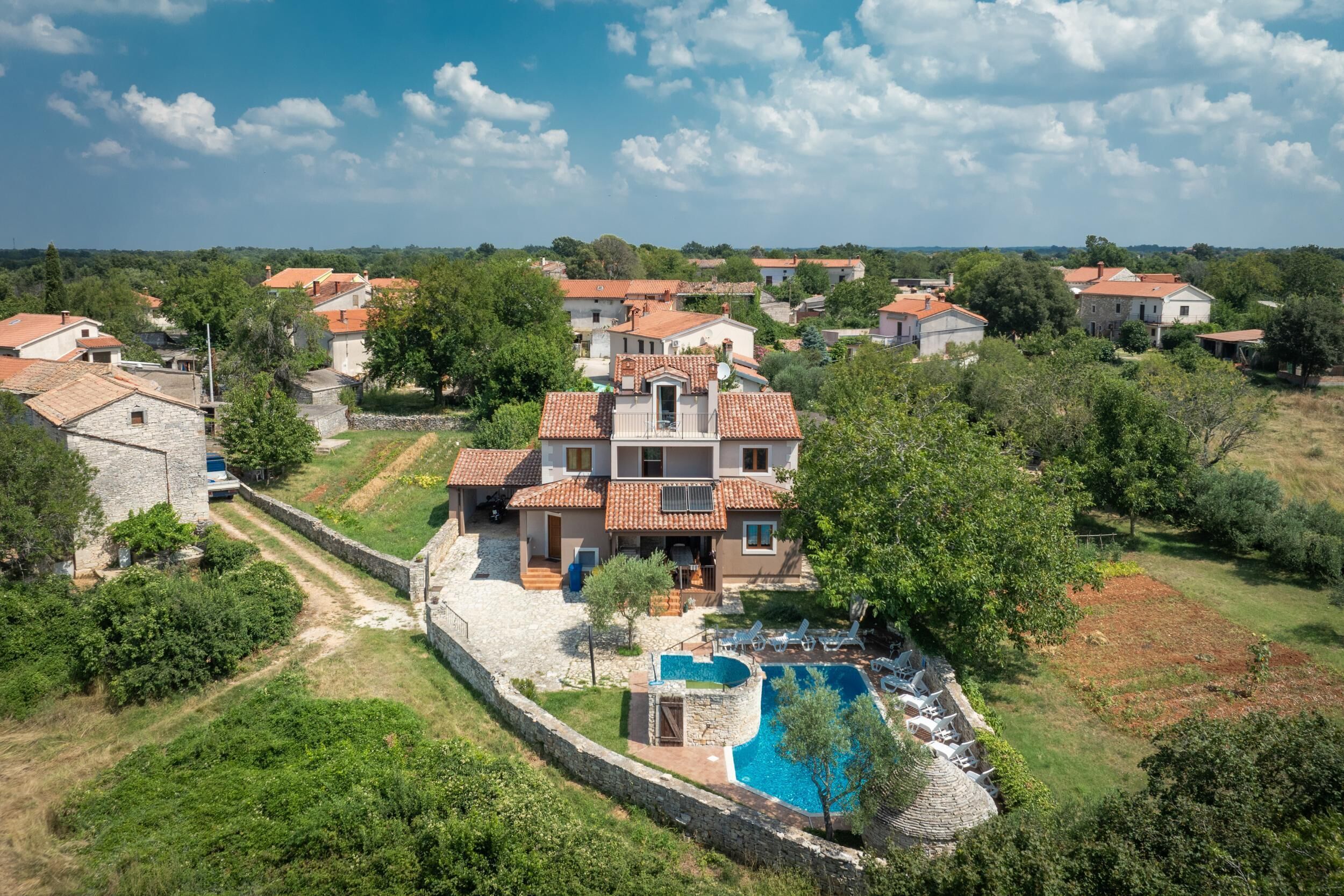 A villa with a swimming pool, surrounded by greenery and other houses.