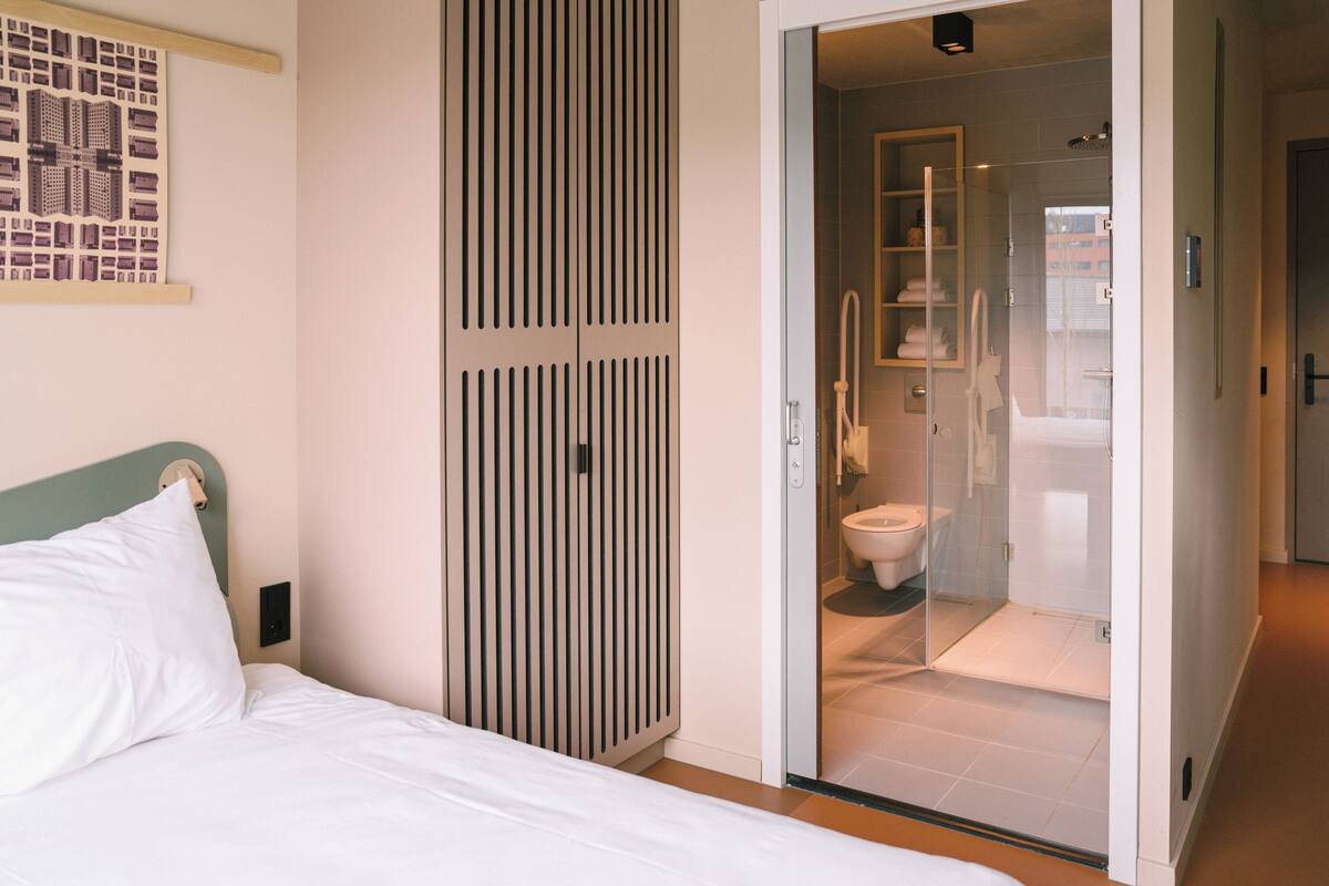 A hotel room with a bed, a wardrobe, and a glass-enclosed shower area.
