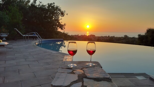 An infinity pool with two wine glasses on a stone ledge, overlooking a sunset and the sea. - Villa with Breathtaking Seaview, Private Swimming Pool & Jacuzzi (Corfu)