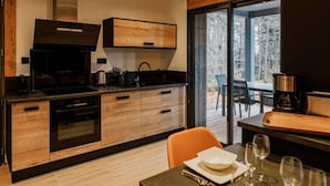Une cuisine moderne avec des meubles en bois, un four encastré et une grande fenêtre donnant sur une zone boisée.