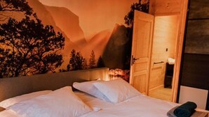 Un lit bien fait, avec du linge de lit blanc, une tête de lit et une fresque murale représentant un paysage montagneux.