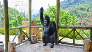 Una estatua de gorila en un recinto de madera con suelo de piedra y vista a un paisaje verde y exuberante.