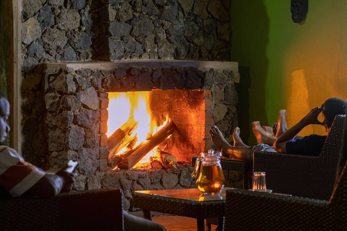 A stone fireplace with a fire, a green wall, and two wicker chairs with people relaxing.