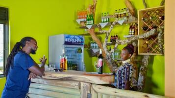 Una zona de bar con mostrador de madera, un refrigerador con el logotipo de BRUHM, estantes con botellas y una estructura decorativa de árbol.