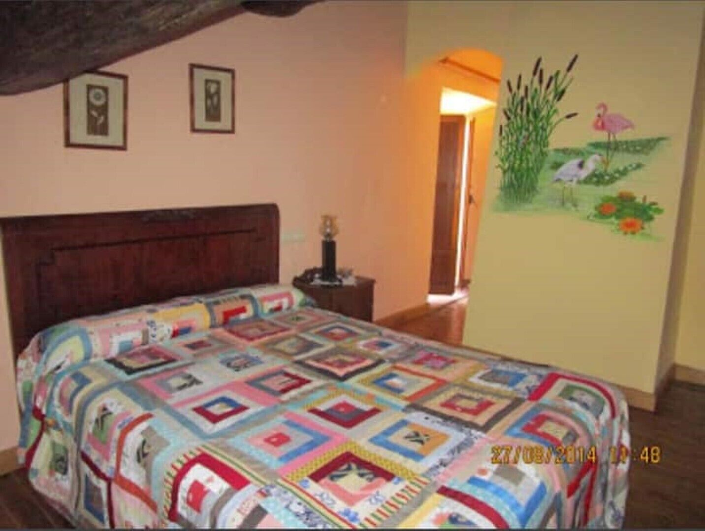 A bedroom with a wooden bed, a nightstand, and a wall with a floral painting.
