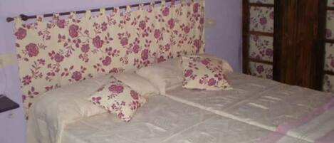 Une chambre à coucher avec une tête de lit à motifs floraux, un lit avec deux oreillers et une porte en bois.