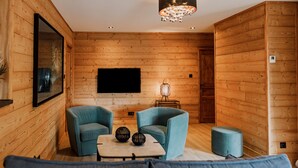 Un salon moderne avec des murs recouverts de panneaux de bois, un téléviseur à écran plat fixé au-dessus d’un canapé et une petite table agrémentée d’objets décoratifs.