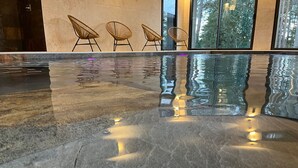 Een modern binnenzwembad met een spiegelende vloer, grote ramen en rieten stoelen langs de muur.